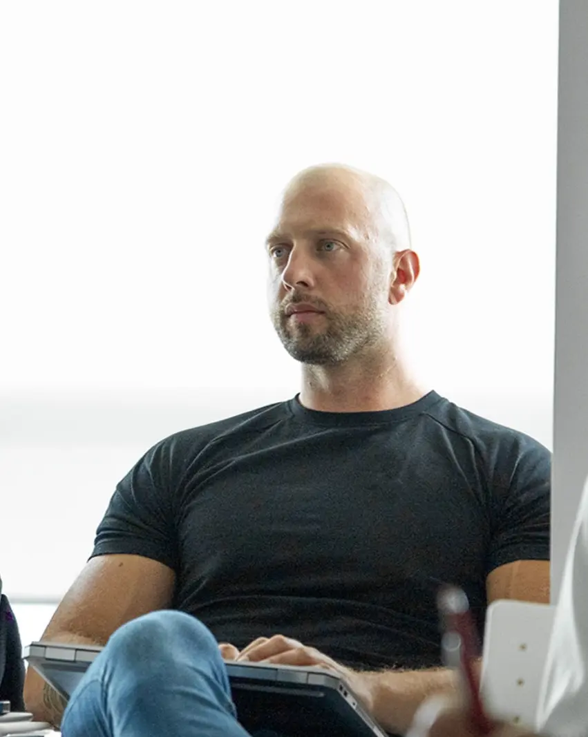 Mike seated with a laptop on his lap, looking off-camera, bright daylight
